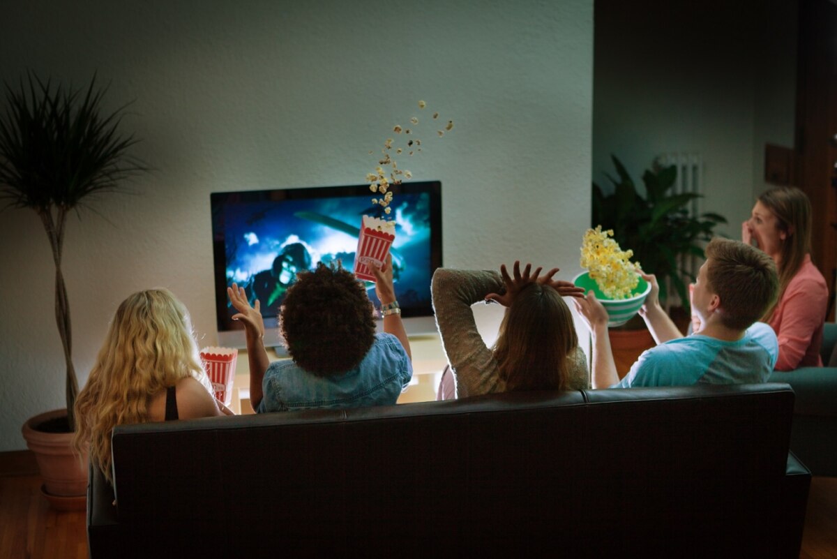 Group Of Young People In Suspense Watching A Scary Movie On TV Together At Home For Halloween. Image On TV Screen Is Photographer's Own.